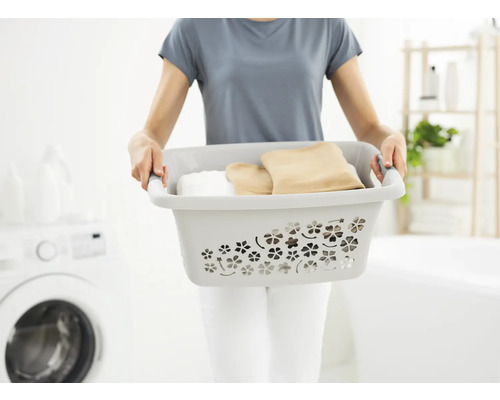 Femme portant un panier à linge rempli de vêtements dans une salle de bain