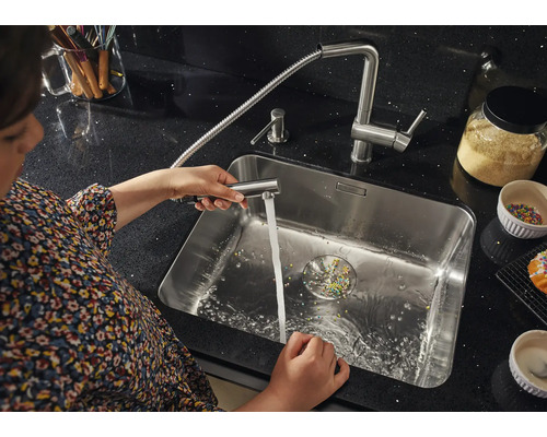 Femme nettoie l''évier avec un robinet de cuisine extensible.