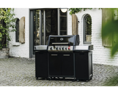 Barbecue à gaz noir avec armoire basse et roulettes à l''extérieur devant un bâtiment en briques blanches.