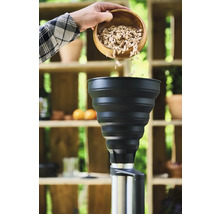 Eine Person schüttet Räucherspäne aus einer Holzschale in einen Smoker.