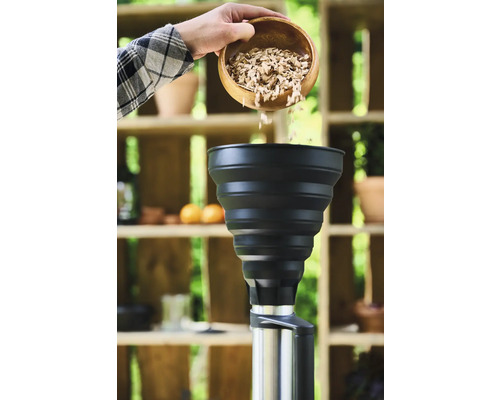 Eine Person schüttet Räucherspäne aus einer Holzschale in einen Smoker.