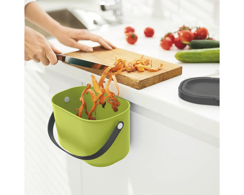 Küchenszene mit grünem Bioabfallbehälter, Schneidebrett und Gemüse