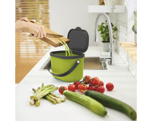 Szene einer Küche mit einem grünen Bioeimer, einer Person, die Gemüseabfälle entsorgt, Tomaten, Gurken und Spargel