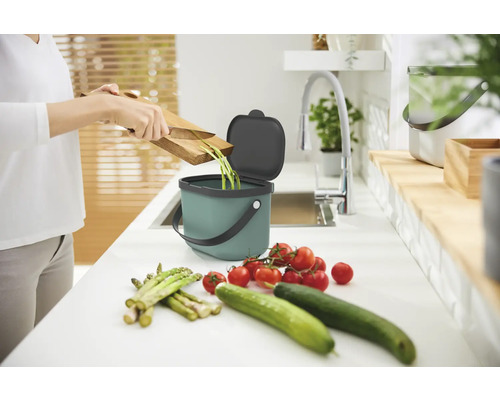 Une personne jette des déchets de légumes dans un bac à compost sur un comptoir de cuisine