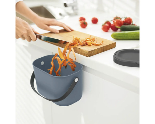 Person schneidet Gemüse und wirft es in einen Abfallbehälter in der Küche.