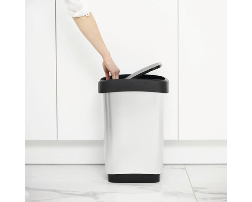 Une personne ouvre une poubelle en métal dans la salle de bain