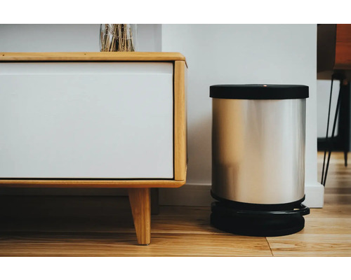 Szenenbild mit einem Treteimer aus Metall und einem weißen Holzschrank