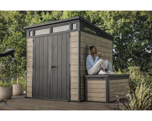 Abri de jardin avec porte double et lanterneau à côté d''un banc en bois sur lequel est assise une femme