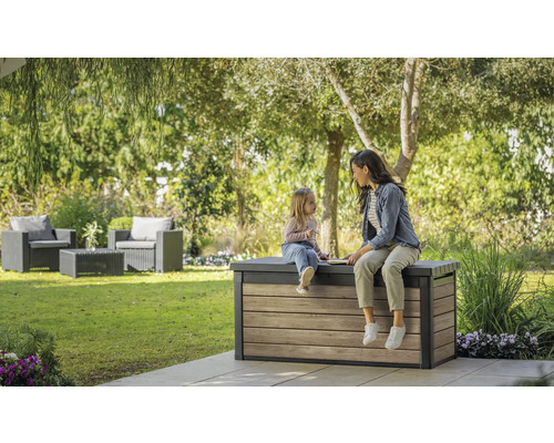 Dans le jardin, une femme et un enfant sont assis sur un coffre de rangement en bois.