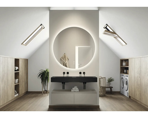 Salle de bain lumineuse dans les combles avec miroir rond éclairé, lavabo, fenêtres de toit et placards intégrés