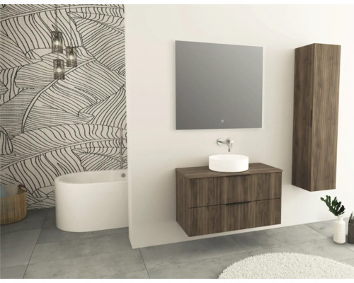 Salle de bains avec baignoire, meuble-lavabo avec miroir et armoire suspendue aspect bois devant un papier peint à motifs