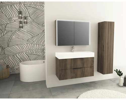 Badezimmer mit Waschtisch, Spiegelschrank und Hochschrank in Holzoptik vor einer Wand mit Blattmuster