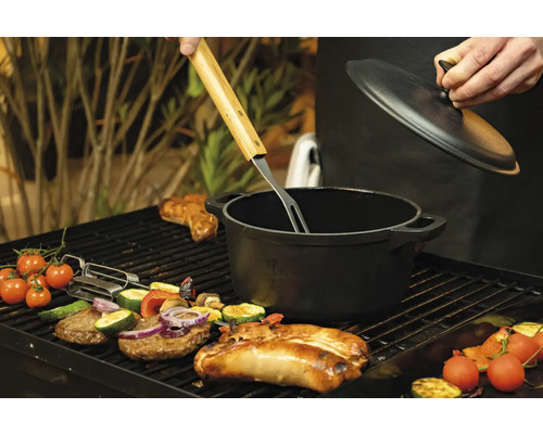 Grillszene mit Grillgut, Gemüse und einem schwarzen Kochtopf mit Deckel