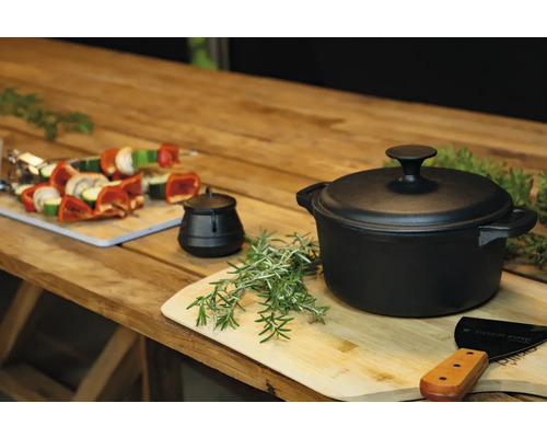 Gusseisentopf mit Deckel auf einem Holztisch mit Gemüsespießen