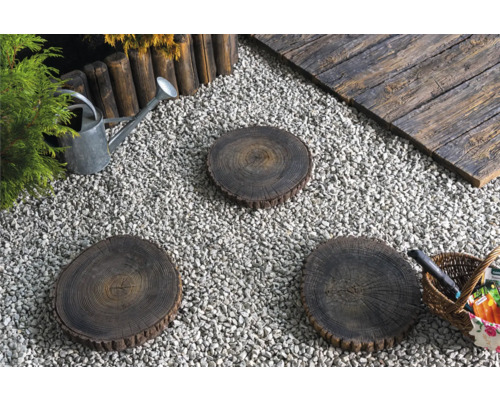 Gartenszene mit Kies, Baumscheiben als Trittsteine, Holzbord, Giesskanne und Korb