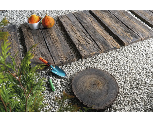 Scène de jardin avec des dalles de chemin en bois, du gravier, une rondelle de souche d''arbre, une pelle, un râteau et des courges.