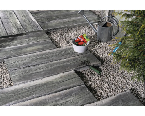 Scène de jardin avec des dalles de chemin dalles aspect bois, du gravier, un arrosoir et des outils de jardin