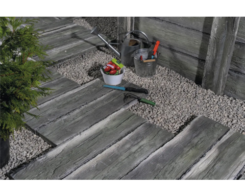 Scène de jardin avec des pas japonais imitation bois, allée en gravier, arrosoir et outils de jardinage