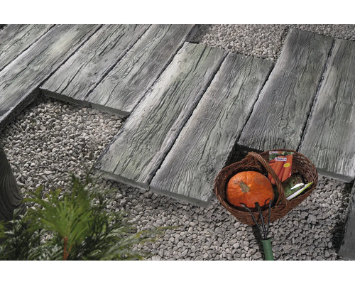 Scène de jardin avec dalles de chemin dalles aspect bois, gravier décoratif et panier contenant des outils de jardinage.