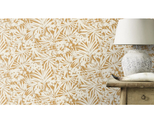 Gros plan d''un mur avec du papier peint botanique, masquant partiellement une lampe et un meuble en bois.