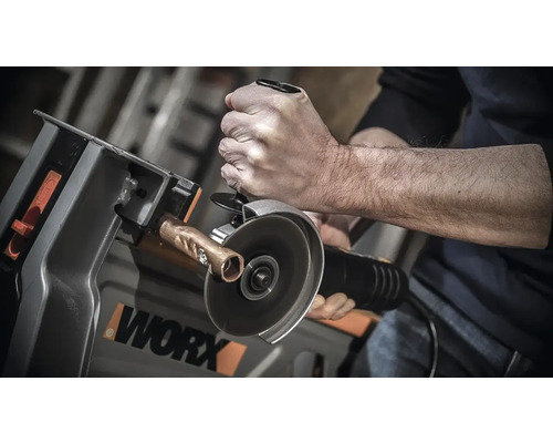 Eine Person schneidet mit einem Winkelschleifer ein Kupferrohr in einer Schneidvorrichtung der Marke Worx.