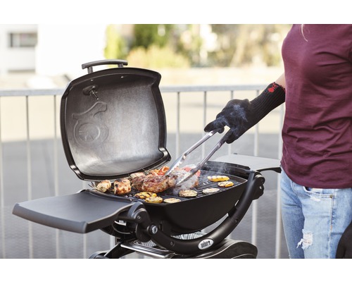 Frau grillt mit Holzkohlegrill Fleisch und Gemüse im Freien.