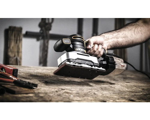 Une personne utilise une ponceuse vibrante de la marque Worx sur une surface en bois.