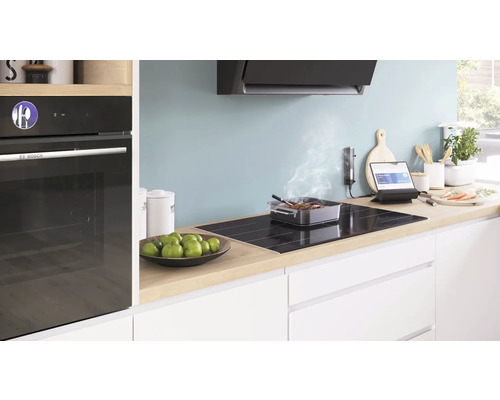 Cuisine moderne avec four intégré, plaque de cuisson, hotte aspirante et ustensiles de cuisine sur le plan de travail.