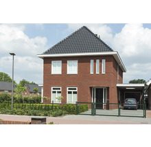 Ein zweistöckiges Einfamilienhaus mit Ziegelmauerwerk, einem dunklen Dach und einem Carport