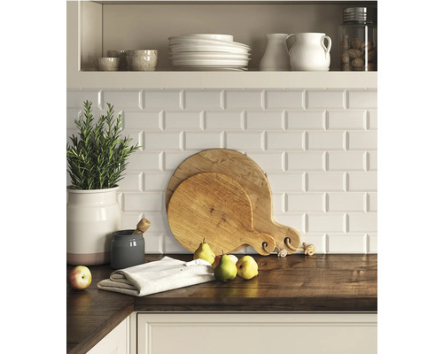 Scène de cuisine avec des planches à découper, de la vaisselle et des herbes aromatiques sur un plan de travail, devant un fond de carreaux blancs.