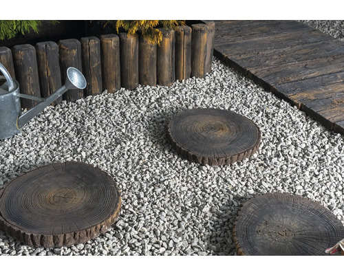 Scène de jardin avec allée de gravier, bordure de parterre en piquets de bois, arrosoir et pas japonais en forme de tronc d''arbre.
