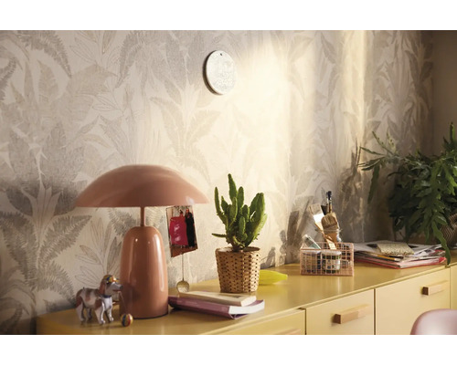 Pièce décorative avec papier peint à motifs, lampe de table et divers éléments de décoration sur une armoire jaune.