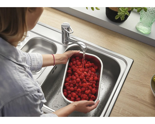 Femme lavant des framboises dans un récipient en acier inoxydable sous un robinet dans un évier en acier inoxydable