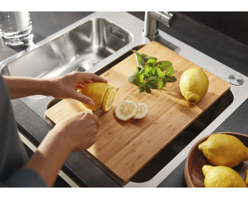 Eine Person schneidet eine Zitrone auf einem Schneidebrett über einer Edelstahlspüle.