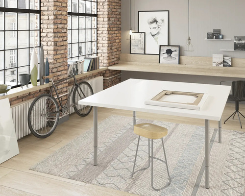Atelier avec table blanche, tabouret et tapis devant un mur de briques