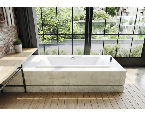 Freistehende Acrylbadewanne auf Betonsockel vor grossem Fenster