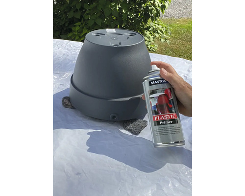 Une personne vaporise un pot de fleurs avec un apprêt pour plastique.