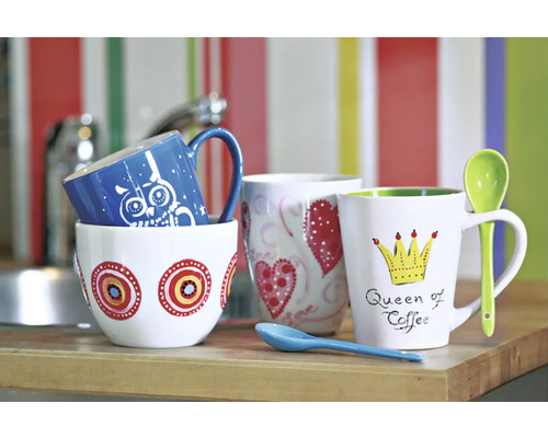 Verschiedene Kaffeebecher mit Motiven auf einer Küchentheke.