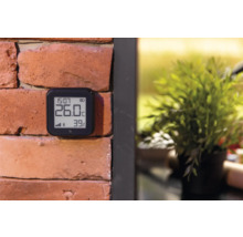Digitales Thermometer an einer Backsteinmauer zur Anzeige von Temperatur und Luftfeuchtigkeit.