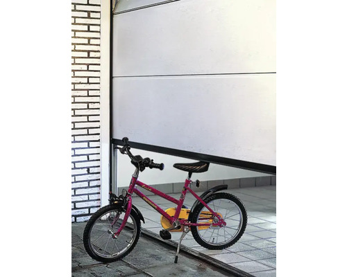 Ein rotes Kinderfahrrad steht vor einem geöffneten Garagentor.