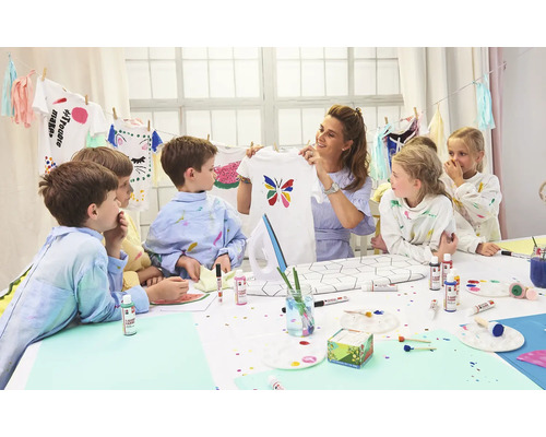 Gruppe von Kindern mit einer Frau, die ein selbstbemaltes T-Shirt mit einem Schmetterling hält, Bastelmaterialien auf einem Tisch