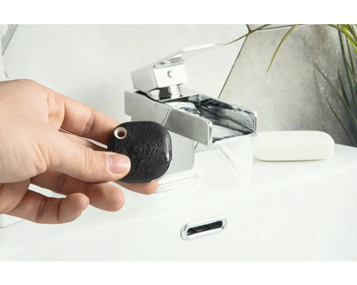 Une main tient un détecteur d''eau noir, carré, devant un lavabo avec robinet