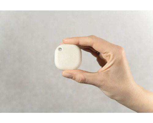 Hand hält einen weissen Ortungsanhänger mit Loch zur Befestigung