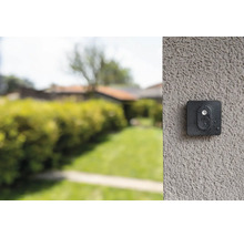 Überwachungskamera an einer Wand mit Garten im Hintergrund