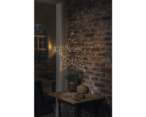 Dekorativer Stern mit LED Beleuchtung, hängend an einer Backsteinmauer über einem kleinen Tisch mit Dekoration.