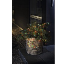 Sapin de Noël décoratif avec des lumières dans un panier métallique devant une maison.