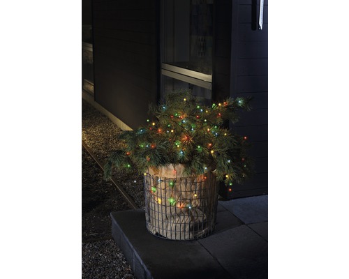 Sapin de Noël décoratif avec des lumières dans un panier métallique devant une maison.