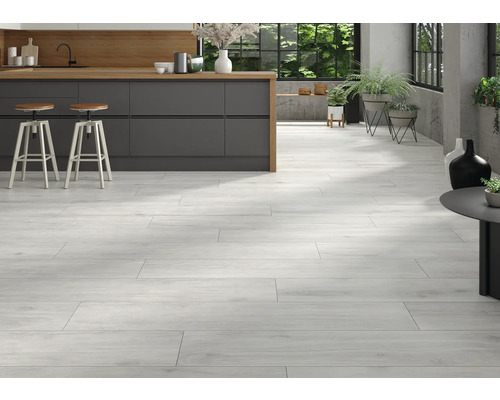 Pièce lumineuse avec carrelage imitation bois, kitchenette et tabourets de bar.