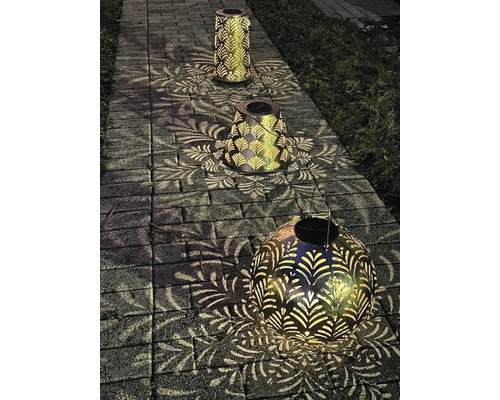 Drei dekorative Solarleuchten aus Metall auf einem Steinweg, die ein Blattmuster auf den Boden werfen.