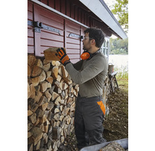 Un homme empile du bois de chauffage contre un mur en bois à côté d''une maison.